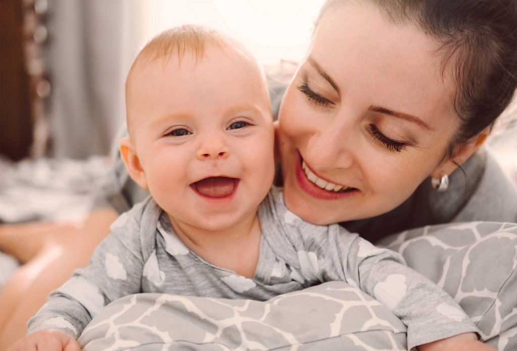 happy smiling mother and baby playing on bed at home